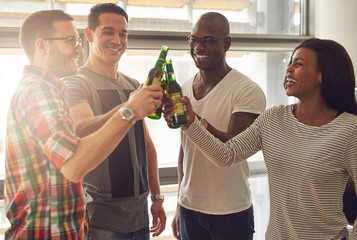 Cheerful people clanging beer bottles in office