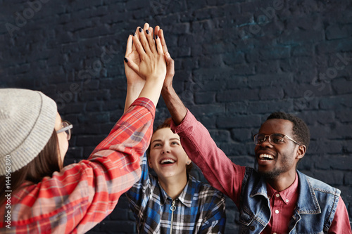 Fotografía International group of stylish young students giving high five at cafe while having lunch, celebrating successful examination at college