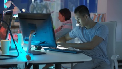 Young mixed ethnicity computer game design team working together in dark office