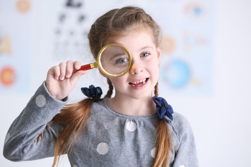 Wall Mural - Cute little girl with magnifier on blurred background