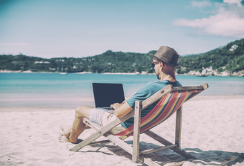 Wall Mural - young hipster man with laptop on tropical beach. travel, vacation, internet, freelance job concept