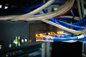 Close up of network internet cables, patch cords connected to black switch router in data center glowing in the dark and cold tone	