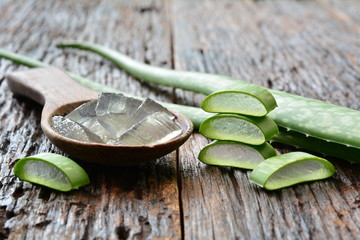 aloe gel on wooden spoon with aloe sliced on wooden table.