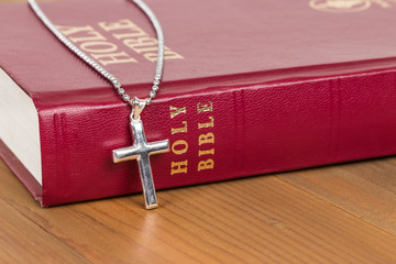 Necklace with silver cross on wooden table and red bible book