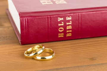 Gold wedding rings on wooden table and red bible book