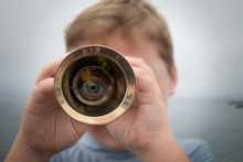 Boy Standing By Ocean Looking Through A Telescope