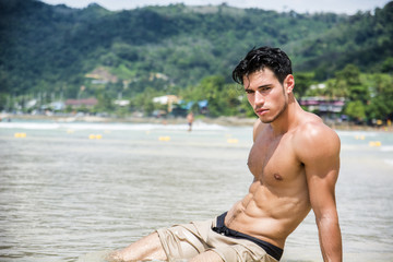 Wall Mural - Handsome young man laying down on a beach in Phuket Island, Thailand, shirtless wearing boxer shorts, showing muscular fit body, looking at camera