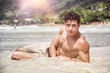 © theartofphoto - Handsome young man laying down on a beach in Phuket Island, Thailand, shirtless wearing boxer shorts, showing muscular fit body, looking at camera