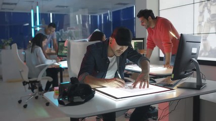  Young creative computer game designer working with colleagues in dark office.