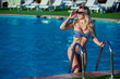 © satyrenko - Beautiful young woman in a pretty swimsuit is standing on a stairs in the swimming pool. She is smiling so wonderful.