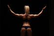 © satyrenko - Beautiful athletic woman in sporty cloths is posing, holding hands up and showing her perfect body, back view isolated on dark background with copyspace