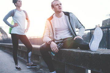 Young athletes relaxing on the bench and resting after hard street running session. Man, woman and urban sport