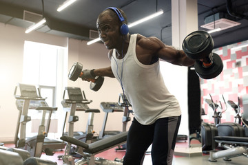 hard workout. Muscular black man doing exercises with dumbbells at gym