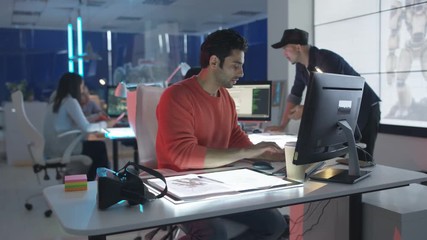  Young creative computer game designer working with colleagues in dark office.