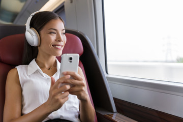 Wall Mural - Woman on train listening to music on smartphone. People lifestyle. Young urban businesswoman using phone app, wireless headphones to listen to audiobook. Asian girl enjoying travel in business class.