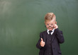 © Ermolaev Alexandr - Boy in a business suit showing thumbs up near empty green chalkboard