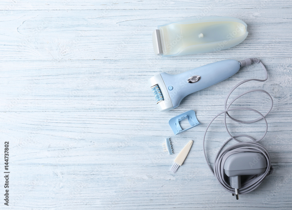 Modern epilator with accessories on wooden background