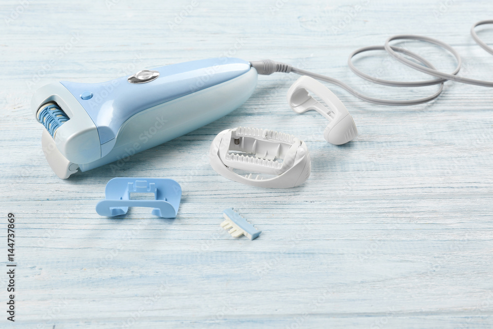 Modern epilator with accessories on wooden background