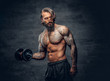 © Fxquadro - Tattooed male doing a biceps workout with dumbbell over dark grey background.