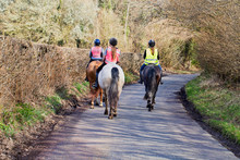 Three Female Horse Riders On Their Horses In A Country Lane Heading Away From The Camera.