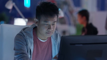  Close up portrait young Asian computer game designer working at his desk