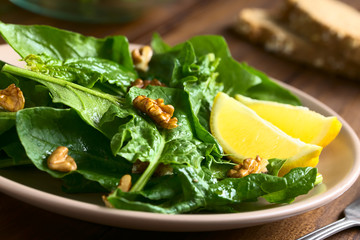 Wall Mural - Fresh spinach and walnut salad with lemon wedges on the side, photographed with natural light (Selective Focus on the walnut in the middle of the image and the one in front of the lemon)