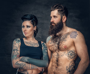 Wall Mural - Portrait of shirtless, tattooed bearded male and brunette female with tattoo ink on her torso.