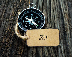compass and paper tag written with task on wooden background.
