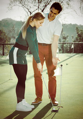 Man teaches woman base golf hit