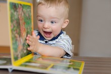 Baby Boy Turns The Page In The Book With Animal. He Is Very Happy And Excited By Watching Pictures. Child Concept.