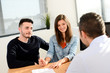 © W PRODUCTION - happy young couple in office with businessman on business buying agreement contract signature