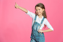 Beautiful Smiling Little Girl In Denim Overalls Showing Thumb Up On Pink