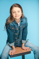 Wall Mural - portrait of little girl smiling and sitting on stool in studio on blue