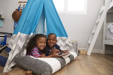 Wall Mural - Two Children Lying In Tent In Playroom With Digital Tablet