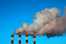 Four Smokestacks Of A Thermal Power Station With Clouds Of Smoke, Air Steam And Blue Sky In A Winter Day. Horizontal Image.