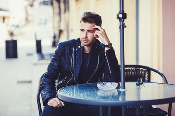 Fashionable man in a jacket sits at a table in the street