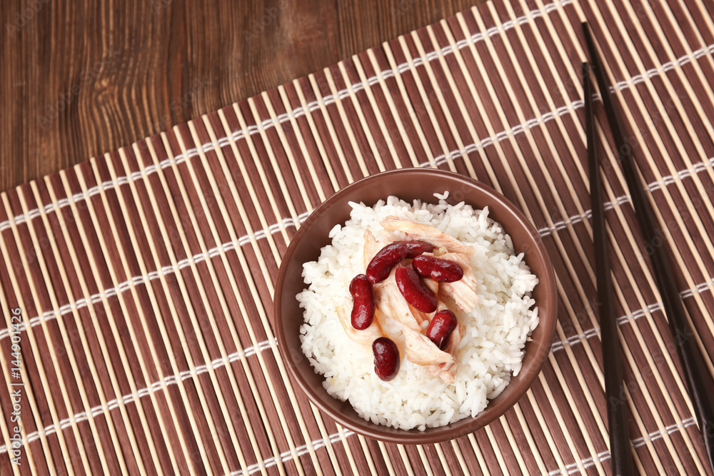 Bowl with tasty chicken, rice and beans on wicker mat