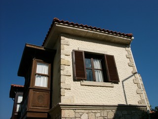 Schöner Altbau mit Fassade aus braunem Holz und naturfarbenem Sandstein vor blauem Himmel im Sonnenschein in der Altstadt von Alacati bei Cesme am Ägäischen Meer in der Provinz Izmir im der Türkei