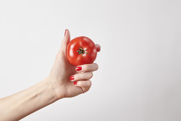 Fresh vegetable tomato in woman hand, fingers with red nails manicure, isolated on white background, healthy lifestyle concept