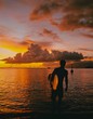 © Tyson Wheatley - Silhouette of man standing in sea with surfboard during sunset