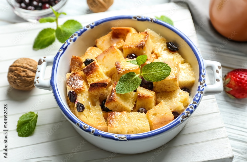 Delicious bread pudding with currant and mint in bowl on wooden board