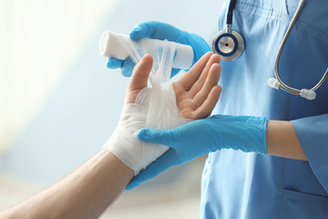 medical assistant applying bandage onto patient's hand in clinic, closeup