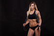 © satyrenko - Beautiful fitness woman is holding a skipping rope. Sporty girl showing her well trained body. isolated on dark background with copyspace