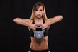 © satyrenko - Young attractive fitness woman is doing exercise with a kettlebell workout. Sporty girl showing her well trained body. isolated on dark background with copyspace