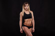 © satyrenko - Beautiful athletic woman in sporty cloths is posing and showing her perfect body isolated on dark background with copyspace