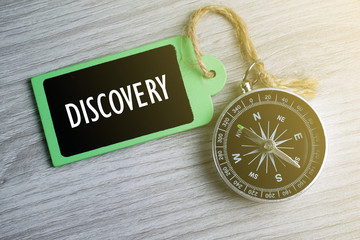 Wall Mural - Compass and wooden tag written with DISCOVERY on grey background.