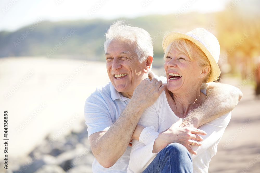 Senior couple relaxing by the sea on sunny day - obrazy, fototapety, plakaty 
