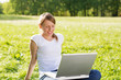 © Goran - Beautiful smiling young woman sitting on a meadow and using her laptop