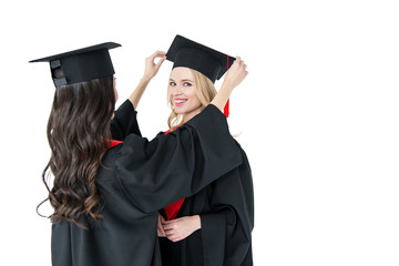 Two young happy women in mortarboards standing together on white background