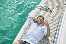 Smiling Man Lying On Deck Of His Motor Yacht Checking Emails